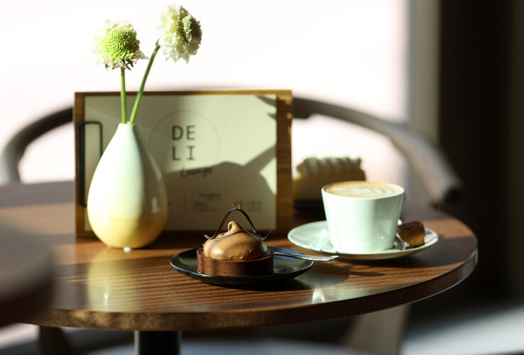 Kaffeetasse mit Törtchen und Vase auf Tisch in der DELI Lounge des ATLANTIC Hotel Heidelberg.