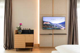 Modernes Hotelzimmer mit TV, Holzschrank, Kaffeemaschine und Pflanze, ATLANTIC Hotel Heidelberg.