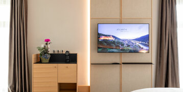 Modernes Hotelzimmer mit TV, Holzschrank, Kaffeemaschine und Pflanze, ATLANTIC Hotel Heidelberg.