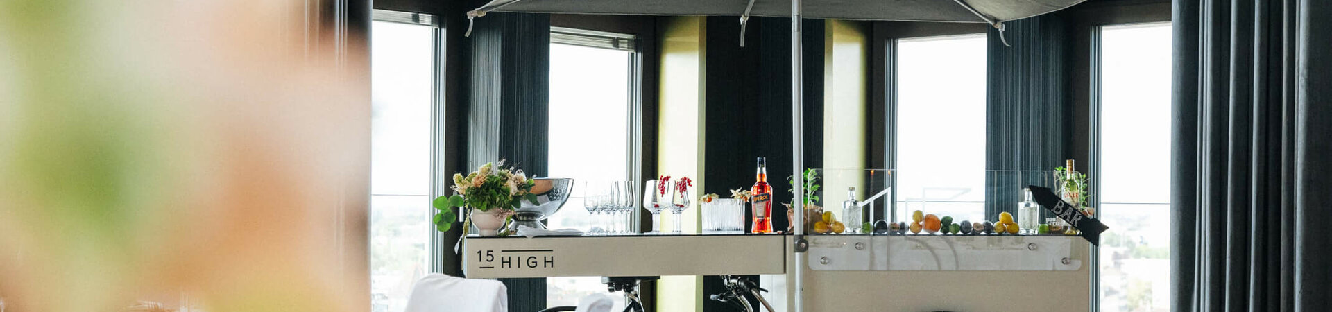 Mobiler Barwagen mit Sonnenschirm in elegantem Hotelraum, dekoriert mit Blumen und Getränken.