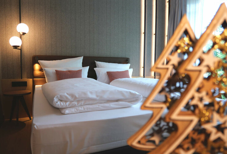 Modernes Hotelzimmer mit Doppelbett, stilvollen Lampen und dekorativem Holzornament im ATLANTIC Hotel Münster.