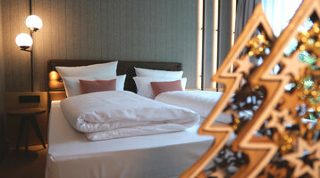 Modernes Hotelzimmer mit Doppelbett, stilvollen Lampen und dekorativem Holzornament im ATLANTIC Hotel Münster.