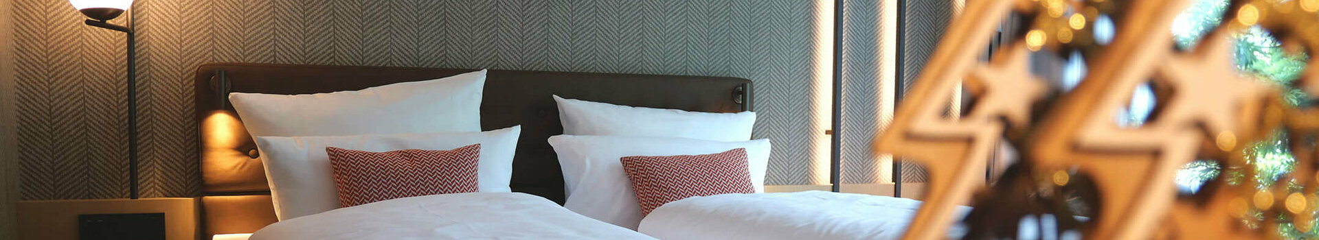 Angebot Adventszeit | ATLANTIC Hotel Münster Modernes Hotelzimmer mit Doppelbett, stilvollen Lampen und dekorativem Holzornament im ATLANTIC Hotel Münster.