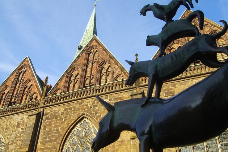 Statue der Bremer Stadtmusikanten vor einer historischen Kirche mit Backsteinfassade und spitzem Turm.