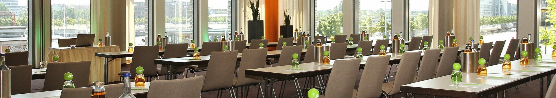 Vorbereiteter Tagungsraum im ATLANTIC Hotel Kiel Moderner Konferenzraum im ATLANTIC Hotel Kiel mit Tischen, Stühlen, Getränken und Blick auf die Stadt durch große Fenster.