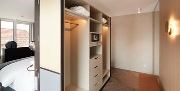 Modern hotel room with open closet, safe, bed and large windows at the ATLANTIC Grand Hotel Bremen.