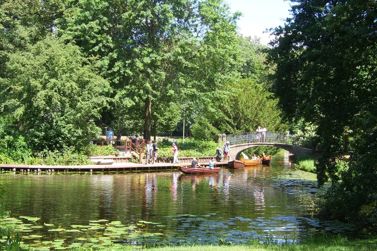 Ruhiger Fluss mit Holzbooten, umgeben von üppigem Grün, Fußgängerbrücke im Hintergrund.