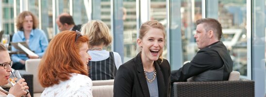 People enjoy drinks on the terrace of the ATLANTIC Hotel Kiel with a view of the city.