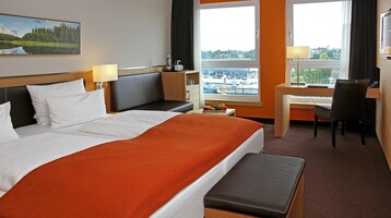 Double bed in the Superior Room with an amazing view in the ATLANTIC Hotel Kiel Modern hotel room at the ATLANTIC Hotel Kiel with double bed, desk, armchair and view of the harbor.