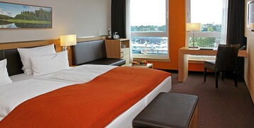 Modernes Hotelzimmer im ATLANTIC Hotel Kiel mit Doppelbett, Schreibtisch, Sessel und Blick auf den Hafen.