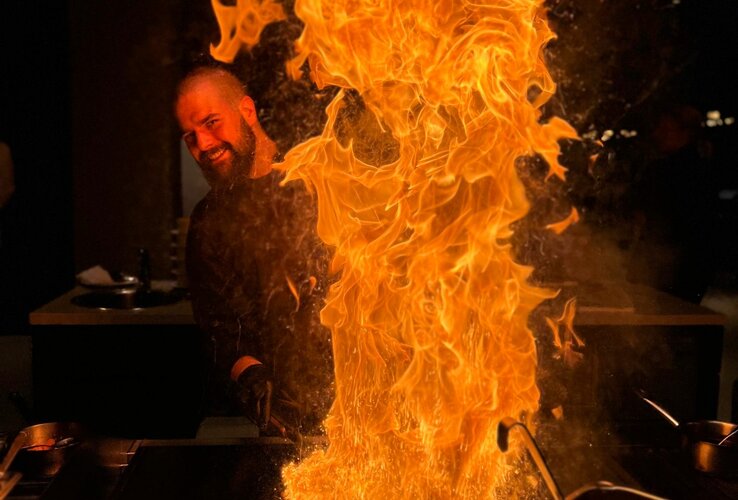 Chef at the grill with a big flame at the ATLANTIC Hotel Münster, puts on a culinary show.