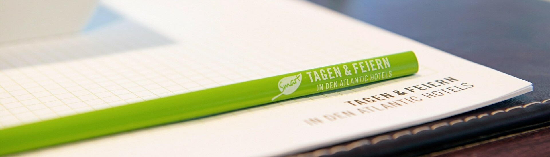 Green pen and pad with "Tagen & Feiern" written on it on a conference table, next to it a glass of water and a bowl.