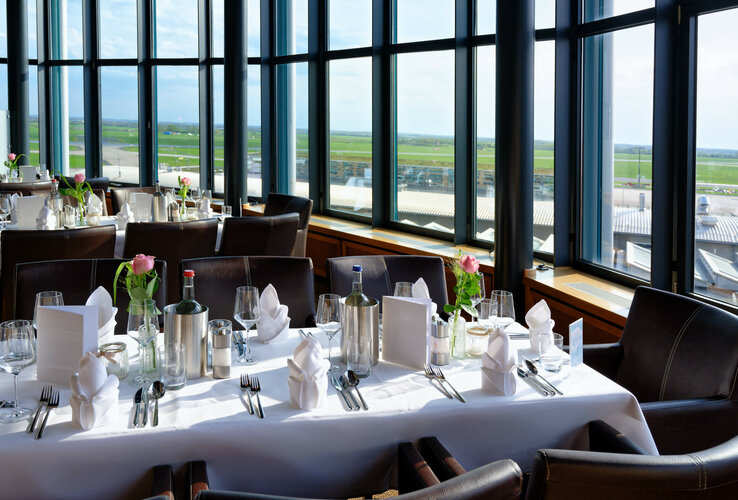 Elegantes Restaurant im ATLANTIC Hotel Airport mit gedeckten Tischen und großem Fensterblick auf das Rollfeld.