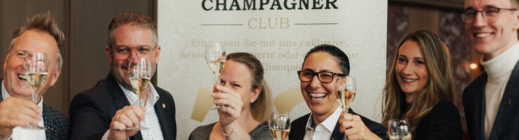 Menschen halten lachend ein Glas Champagner.