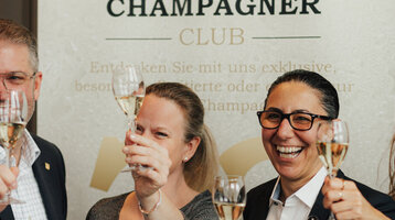 Menschen halten lachend ein Glas Champagner.