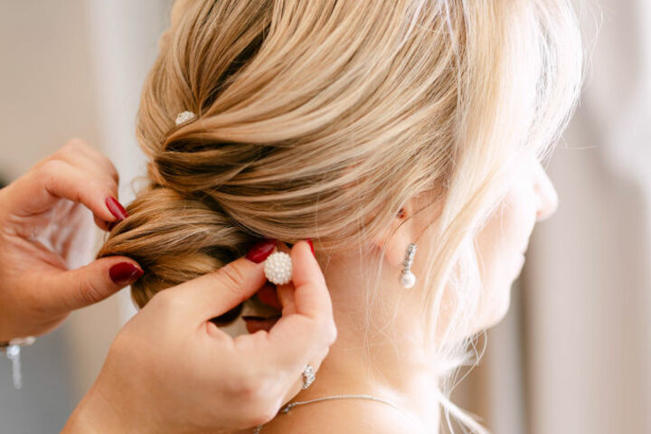 A person puts a hair clip in the wedding hairstyle of a woman with blonde hair.