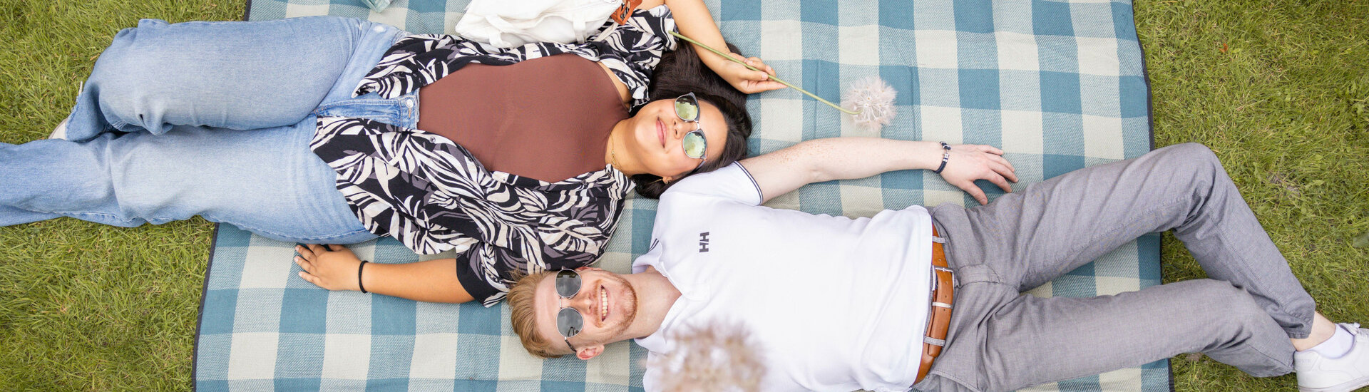 Freizeit im Grünen genießen im ATLANTIC Hotel Landgut Horn  Ein Paar liegt lächelnd auf einer blaukarierten Picknickdecke