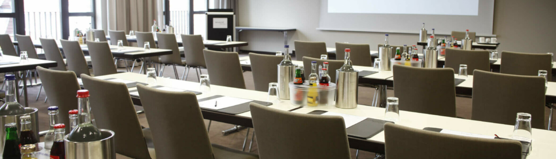 Moderner Konferenzraum im ATLANTIC Hotel Lübeck mit Tischen, Stühlen und Getränken, bereit für Meetings.