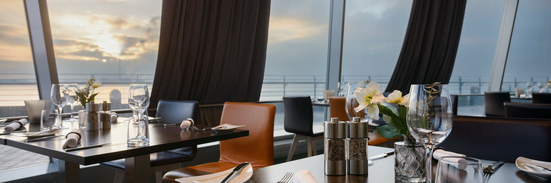 Modernes Restaurant mit gedeckten Tischen und Meerblick bei Sonnenuntergang im ATLANTIC Hotel Sail City, Bremerhaven.