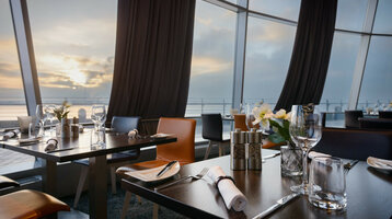 Modernes Restaurant mit gedeckten Tischen und Meerblick bei Sonnenuntergang im ATLANTIC Hotel Sail City, Bremerhaven.
