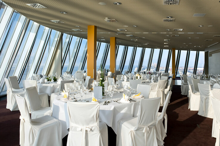 Elegantes Restaurant mit gedeckten Tischen, weißen Stuhlhussen und Panoramafenstern mit Stadtblick.