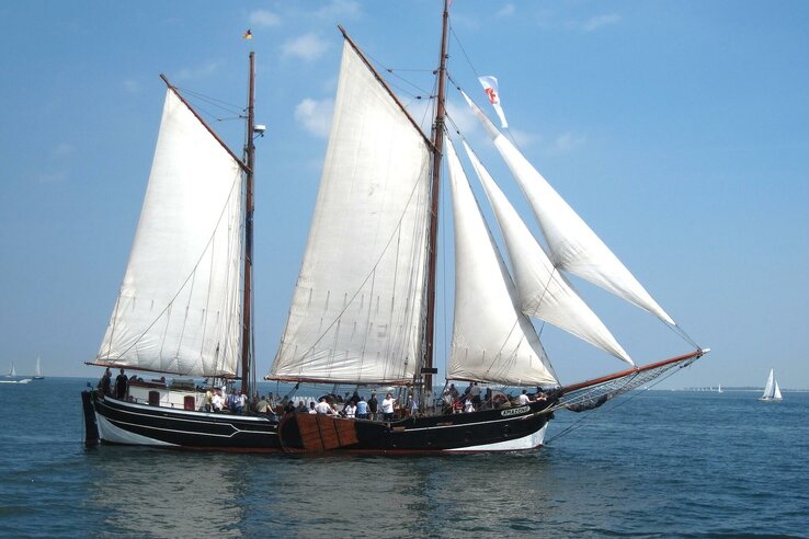 Großes Segelschiff mit weißen Segeln auf der Ostsee, blauer Himmel, Menschen an Bord, nahe dem ATLANTIC Grand Hotel Travemünde.