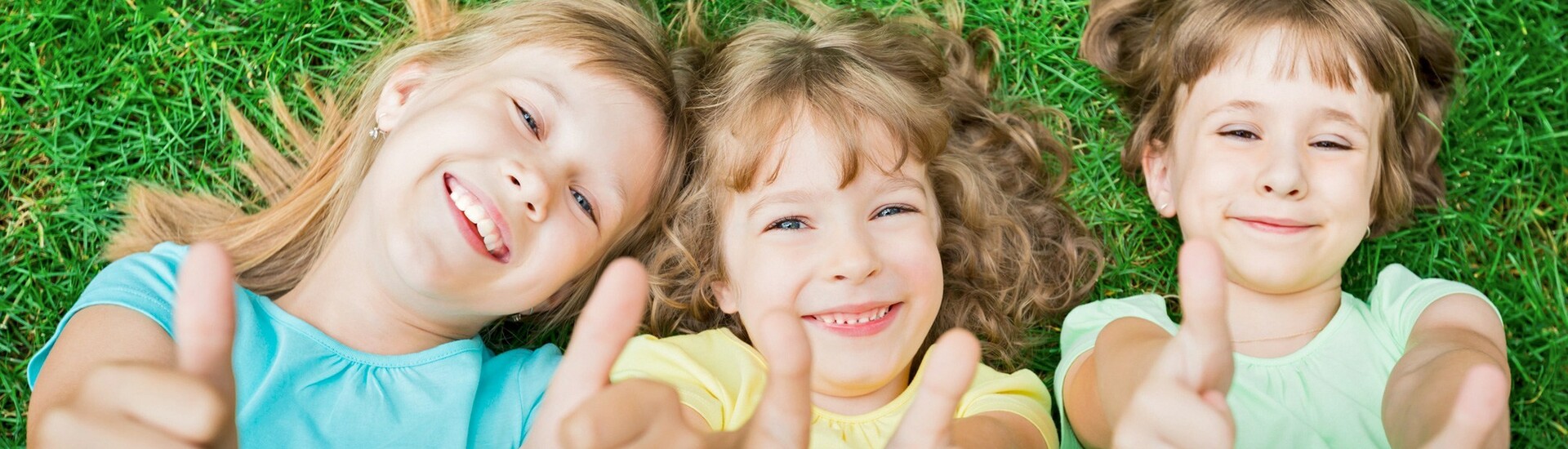 Kinder auf der Wiese vor dem ATLANTIC Hotel Universum Bremen Drei lachende Kinder liegen auf Gras und zeigen Daumen hoch.