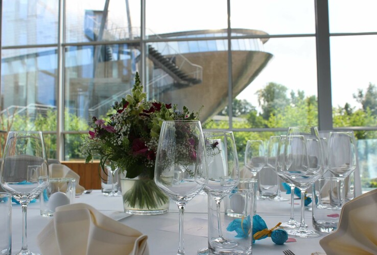 Elegant gedeckter Tisch mit Blumenarrangement, Blick auf modernes Gebäude durch große Fenster im ATLANTIC Hotel Universum.