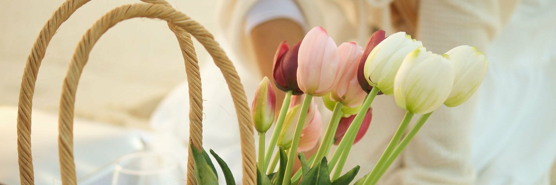 ATLANTIC Hotel Wilhelmshaven Special Happy Easter A basket of colorful tulips stands on a picnic blanket on the beach.