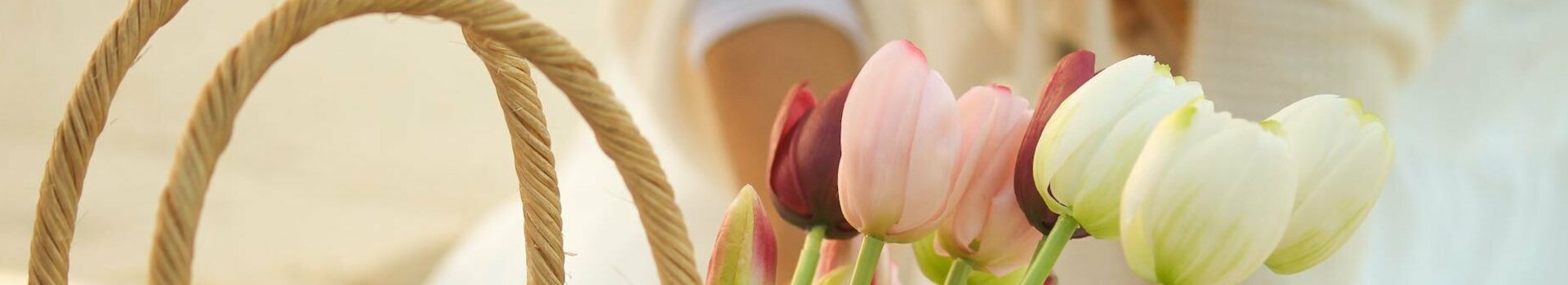 Ein Korb mit bunten Tulpen steht auf einer Picknickdecke am Strand.
