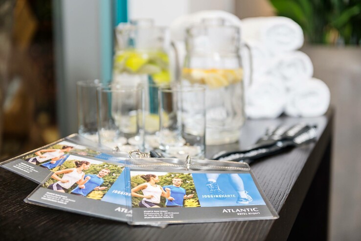 Jogging cards, glasses, jugs of water with lemon and towels on a table in the ATLANTIC Hotel Airport Bremen.