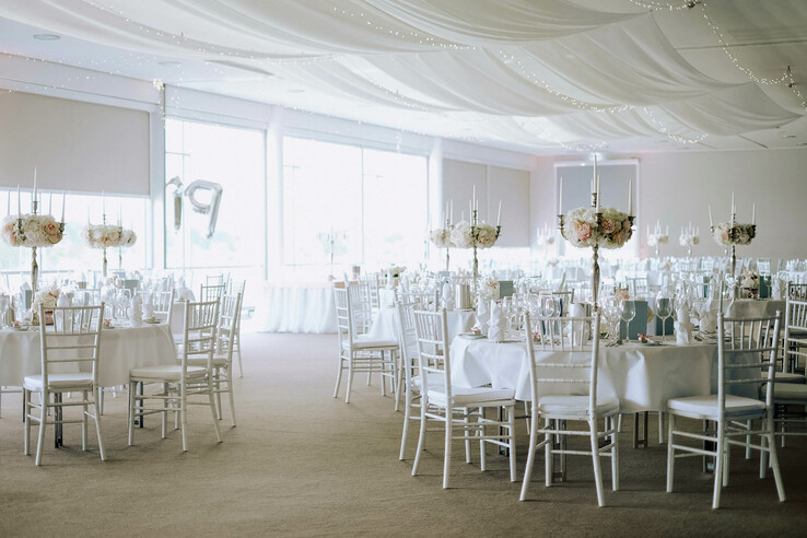 Eleganter Bankettsaal mit weißen Stühlen, dekorierten Tischen und festlicher Beleuchtung im ATLANTIC Hotel Galopprennbahn.