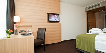 Modernes Hotelzimmer mit Schreibtisch, Stuhl, Flachbildfernseher und Bett mit grünem Überwurf im ATLANTIC Hotel Kiel.