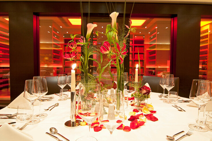 Elegantly laid table at the ATLANTIC Hotel Kiel, with flowers, candles and wine glasses, against a red background.