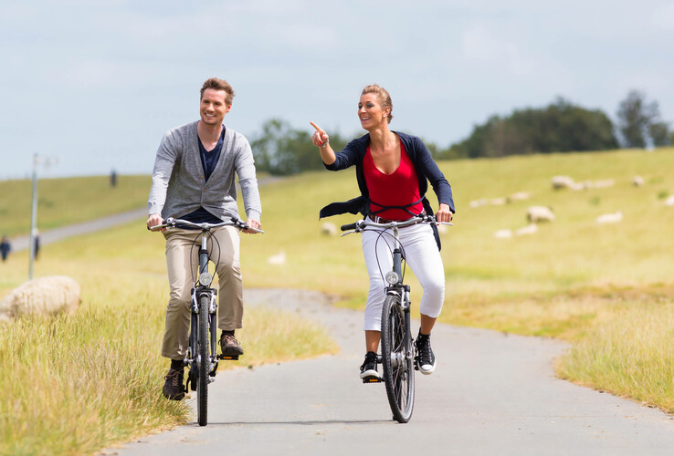 Couple riding happily on bicycles through green countryside near the ATLANTIC Grand Hotel Travemünde.