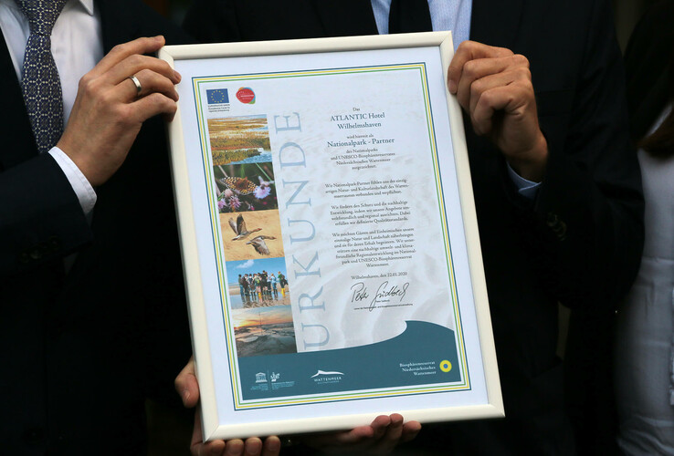 Zwei Personen halten eine gerahmte Urkunde des ATLANTIC Hotels Wilhelmshaven als Nationalpark-Partner.