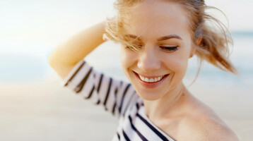 Smiling woman on the beach, wearing a striped shirt, wind in her hair, sunny weather.