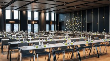 ATLANTIC Hotel Heidelberg Ballroom with parliamentary seating Modern conference room at the ATLANTIC Hotel Heidelberg with rows of tables and chairs, large windows and elegant lighting.