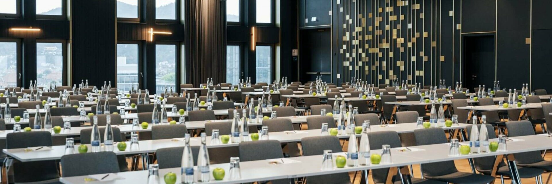 Moderner Konferenzraum im ATLANTIC Hotel Heidelberg mit Reihen von Tischen und Stühlen, großen Fenstern und eleganter Beleuchtung.