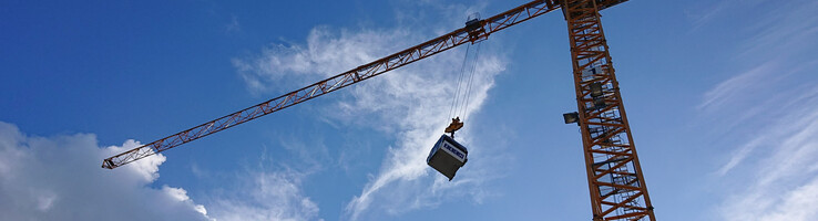 Kran hebt Container vor blauem Himmel mit Wolken.