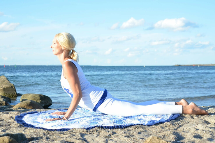 Person macht Yoga am Strand vor dem Meer, bei sonnigem Wetter.