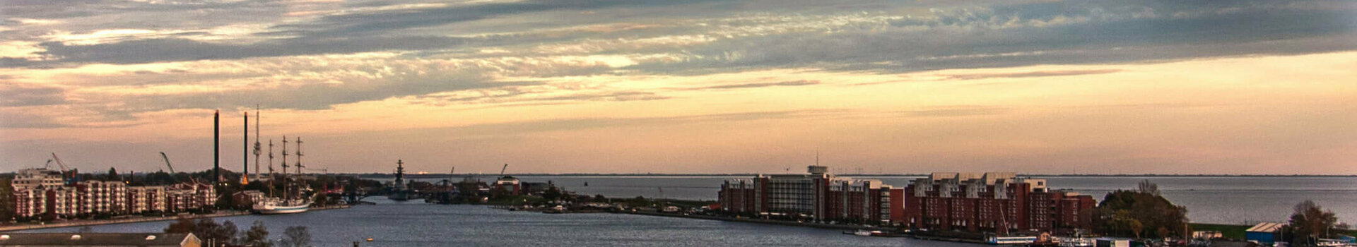 Blick von einem Balkon auf einen Fluss bei Sonnenuntergang, mit Stadtgebäuden und Wolken am Horizont.