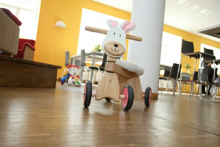 Holzspielzeug in Tierform auf Holzboden in hellem Raum mit gelber Wand und modernen Möbeln. © SOS Kinderdorf