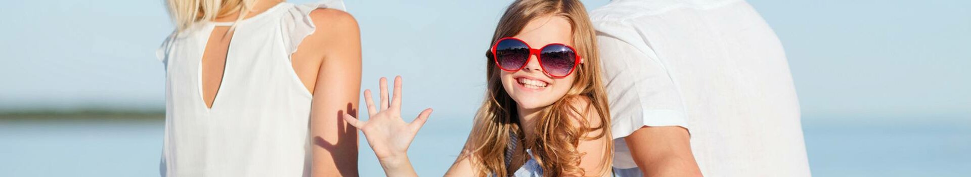 Family at the beach close to Kiel Family on the beach, sitting on a blanket, smiling child with red sunglasses, blue sky in the background.