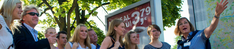Gruppe von Menschen bei einer Stadtführung in Kiel, mit einer Karte und Bäumen im Hintergrund.