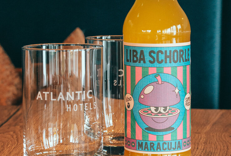 A yellow bottle of LIBA Schorle stands next to a glass bearing the words ‘ATLANTIC Hotel Münster’.