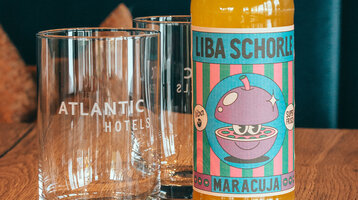 Eine gelbe Flasche LIBA Schorle steht neben einem Glas auf dem "ATLANTIC Hotel Münster" steht.