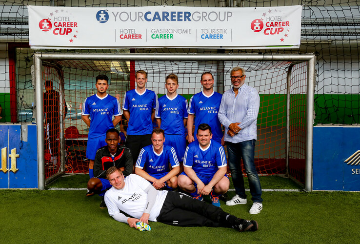Fußballteam des ATLANTIC Hotel Sail City posiert in blauen Trikots vor einem Tor auf einem Indoor-Spielfeld.
