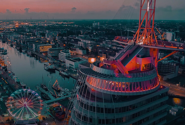 EDM meets Classic in ATLANTIC Hotel Sail City Blick auf das ATLANTIC Hotel Sail City in Bremerhaven bei Dämmerung, mit beleuchtetem Hafen und Riesenrad im Hintergrund.