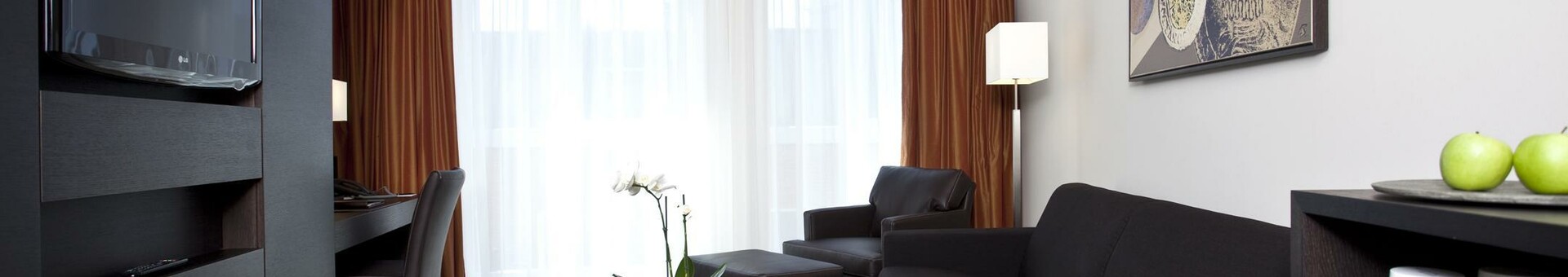 Modern hotel room with black sofa, coffee table, TV, desk, artwork on the wall and large windows.